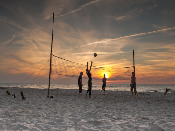 Weitläufiger Strand mit Volleyballspielern im Sonnenuntergang