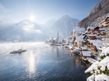 Hallstättersee im Winter mit schneebedeckten Häusern an der Küste und Ausflugsdampfer