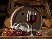 Glas Rotwein mit Trauben und Holzfass im Hintergrund